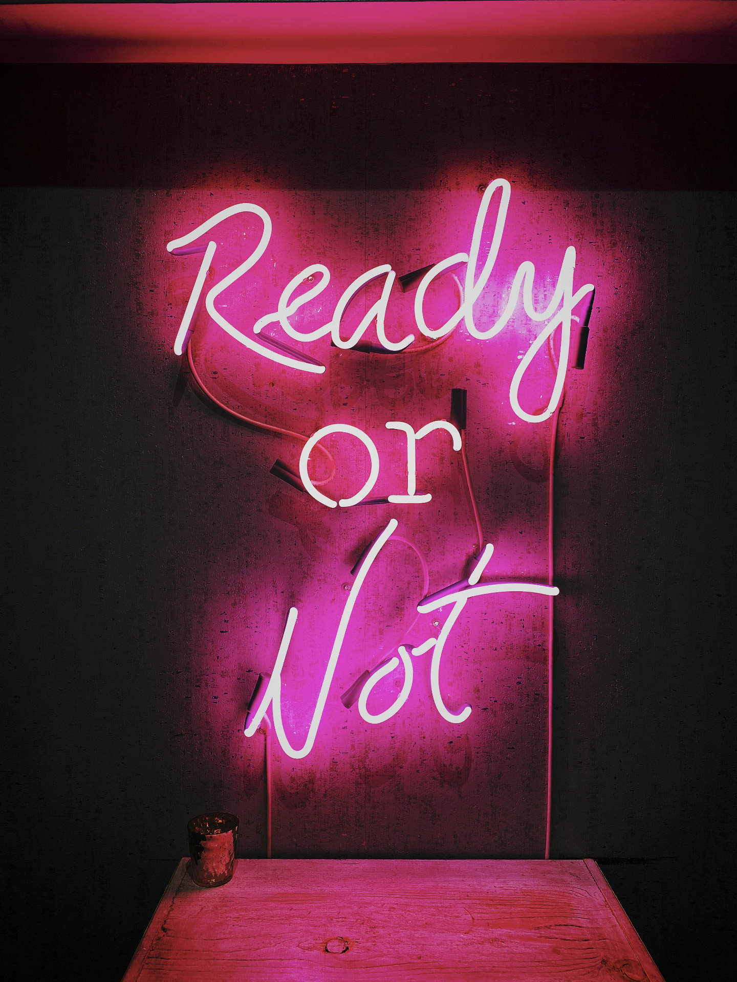 Pink neon sign glowing on a dark wall reading Ready or Not